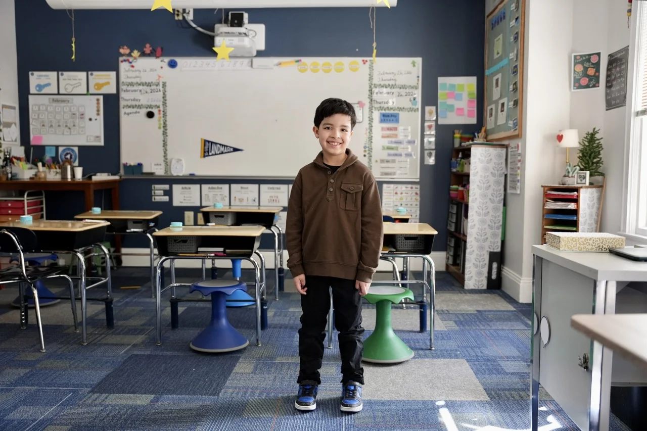 young boy standing in small classroom with six desks